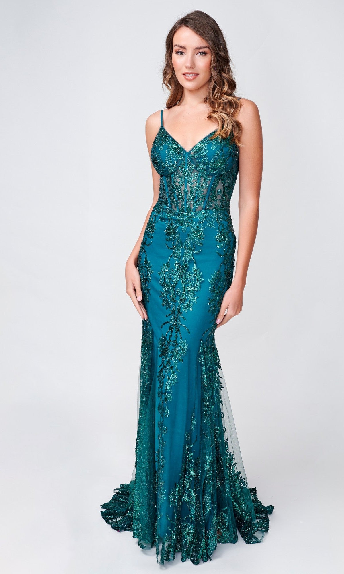 A woman stands against a plain light background wearing the Nina Canacci 1562, a teal, floor-length formal mermaid dress with lace detailing and thin straps.